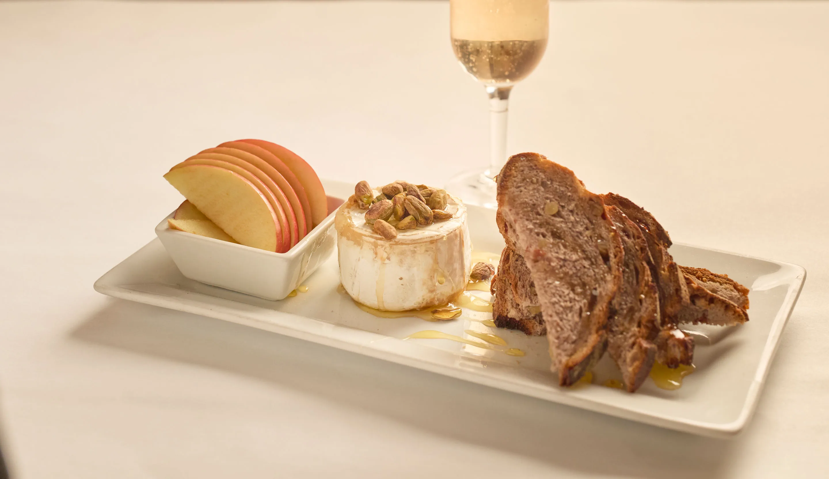 Baked brie topped with nuts and honey, served with sliced apple, toasted bread and a glass of sparkling wine