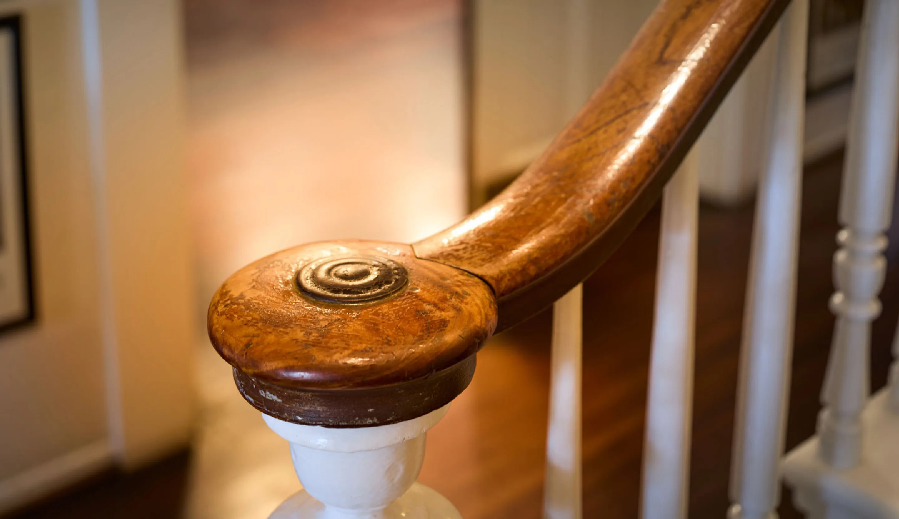 Close-up of a polished wooden stair rail curling into a carved newel above white spindles