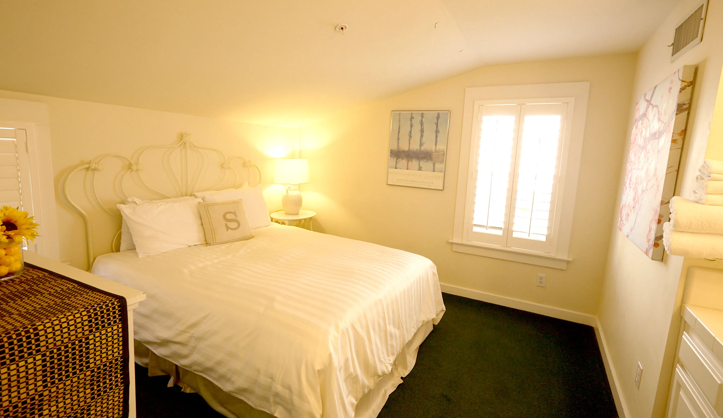 Room 2 at the Swiss Hotel beneath its sloped ceiling, with a white queen bed, a curved white headboard and a shuttered window