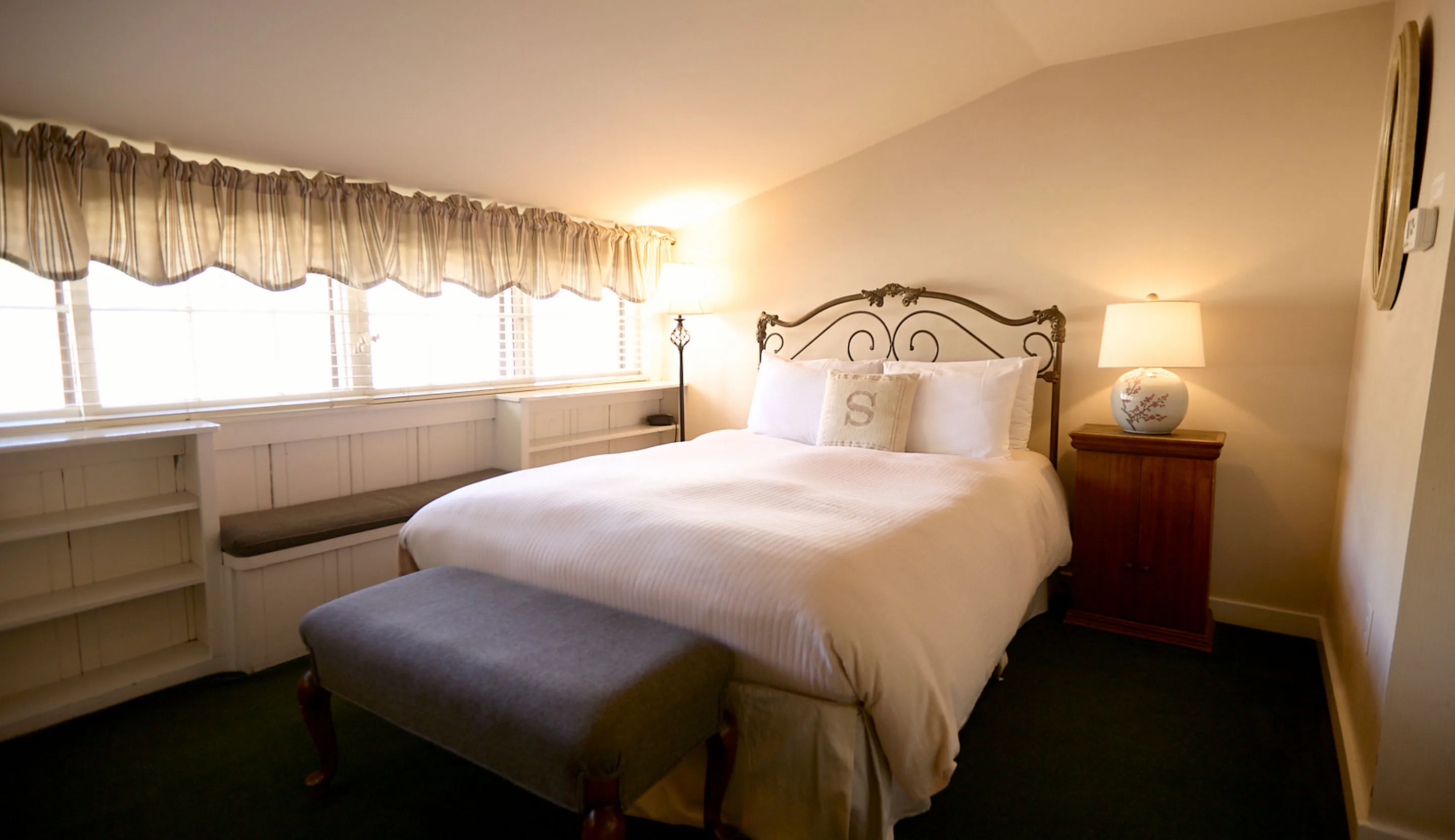 Room 3 at the Swiss Hotel, with a white queen bed and wrought-iron headboard, a bench at its foot and a long window seat beneath a valance